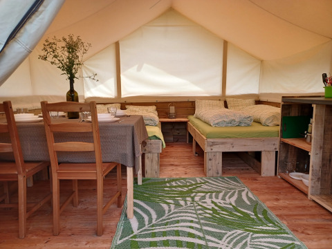 Interior de tienda safari con camas, mesa de comedor y zona de cocina en Camping Sretanwolf en Croacia.