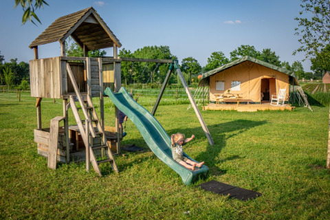 Kinder spielen auf einem Spielplatz neben einem Safarizelt im Ferienpark Hoeve Klein Haneveld in Nordbrabant.