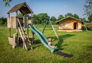 Bambini che giocano su un parco giochi in legno vicino a una tenda glamping a Hoeve Klein Haneveld in Brabante Settentrionale.