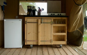 Piccola cucina in una tenda safari con mini frigo, mobile in legno, fornello a gas e utensili da cucina.