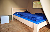 Interior de una tienda safari con una cama de madera, ropa de cama azul y una mesita de noche moderna.