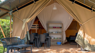 Foto af en safari-telt med en overdækket terrasse, plastikmøbler og udsigt til både sove- og spiseplads.