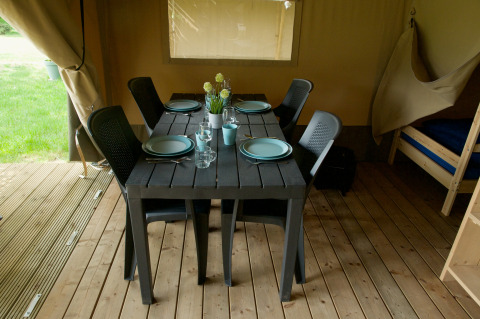 Table à manger dans une tente safari, dressée pour quatre personnes avec assiettes, verres et chaises.