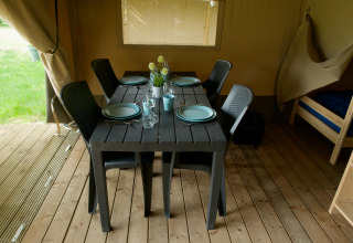 Eettafel in een safaritent met vier borden, glazen, kunststof stoelen en houten vloer, sfeervolle setting.