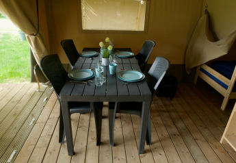 Table à manger dans une tente safari, dressée pour quatre personnes avec assiettes, verres et chaises.