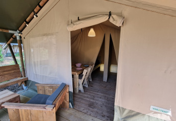 Tenda safari con arredi in legno, area soggiorno e pranzo aperta, spazio letto visibile sullo sfondo.