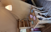 Interior of a safari tent featuring rustic wooden furniture, dining table, chairs, dishes, and a lamp.