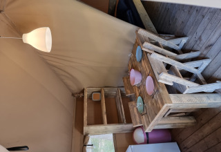 Interior de tienda safari con muebles rústicos de madera, mesa, sillas, vajilla y lámpara encendida.