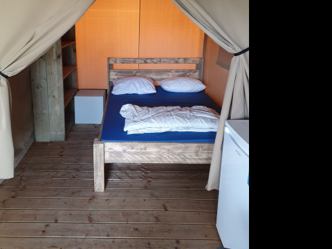 Vista interior de una tienda safari en Camping la Roche, Bélgica, con suelo de madera, cama y muebles.