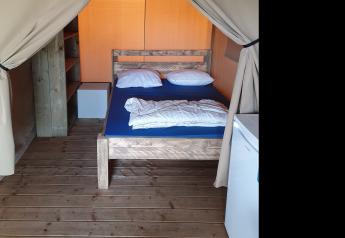 Vista interna di una tenda safari al Camping la Roche in Belgio con pavimento in legno, letto e mobili.