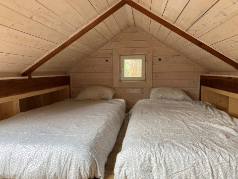 Accogliente stanza mansardata con due letti singoli in Stuga glamping presso Småland Miniglamping, Svezia.