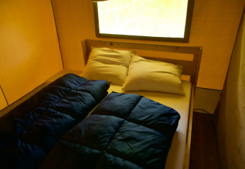 Vista interior de una tienda safari con una cama doble, almohadas y sacos de dormir bajo una gran ventana.