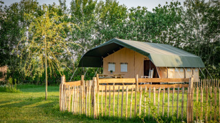 Tienda de safari en Hoeve Klein Haneveld rodeada de árboles verdes y una cerca de madera en la naturaleza.