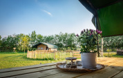 Vista desde una terraza hacia una tienda safari en Hoeve Klein Haneveld, Países Bajos, con flores sobre la mesa.