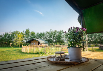 Vista desde una terraza hacia una tienda safari en Hoeve Klein Haneveld, Países Bajos, con flores sobre la mesa.
