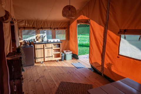 Vista interior de una acogedora tienda safari con suelo de madera y cocina en Hoeve Klein Haneveld, Países Bajos.