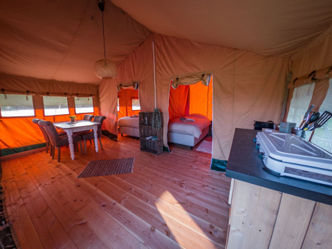 Vista interna di una tenda safari di lusso con pavimento in legno, tavolo da pranzo, letti e angolo cottura.