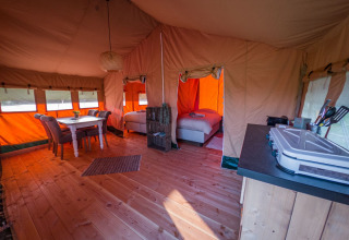 Vista interna di una tenda safari di lusso con pavimento in legno, tavolo da pranzo, letti e angolo cottura.