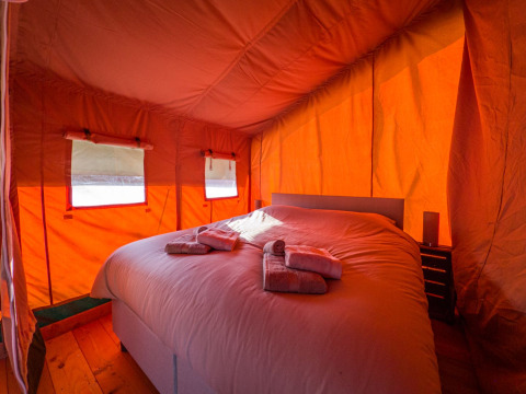 Vista interior de una cómoda tienda safari con una gran cama y toallas en Hoeve Klein Haneveld, Países Bajos.