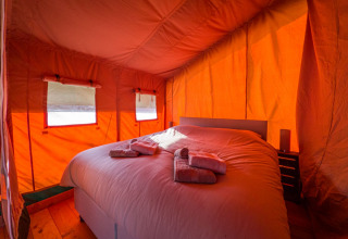 Vista interior de una cómoda tienda safari con una gran cama y toallas en Hoeve Klein Haneveld, Países Bajos.