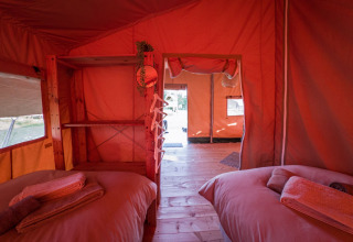 Binnenzicht van een safaritent met twee bedden, houten vloer en open uitgang in Nederland.