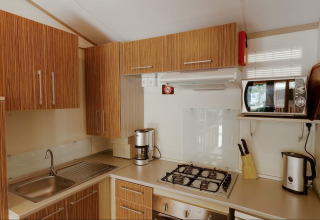 Cocina moderna de glamping en SunLodge Maple con encimera de gas, armarios de madera y microondas.