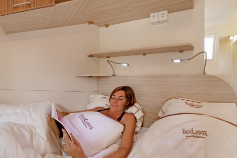 Vrouw relaxt in bed en leest een boek in een SunLodge Maple glamping accommodatie met gezellige verlichting.