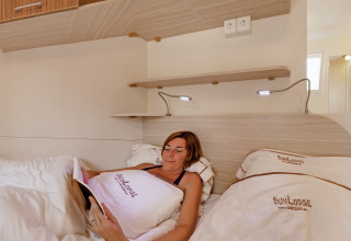 Mujer relajándose en la cama y leyendo un libro en un alojamiento glamping SunLodge Maple con luz acogedora.