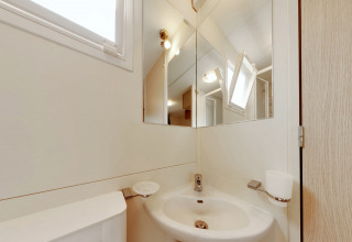 Baño moderno de SunLodge Maple glamping con espejo, lavabo, ventana y paredes de color claro.