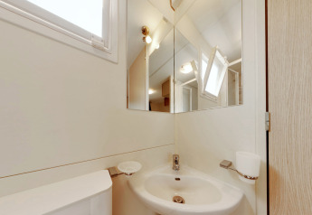 Bagno moderno nella sistemazione glamping SunLodge Maple con specchio, lavabo, finestra e pareti chiare.
