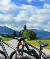 Two bicycles stand on a country road with green fields and mountains near St. Peter am Kammersberg, Austria.