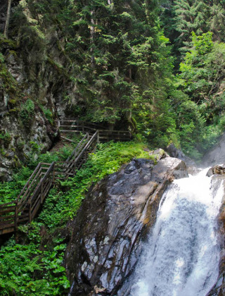 Waterfall and lush greenery near St. Peter am Kammersberg, Styria, Austria, with visitors on wooden paths.
