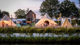 Evening at Happy Harbor Tent + Bathroom, Holiday Park Mölke, Netherlands, with glowing teepee tents.