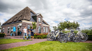 Parque vacacional en Holanda Septentrional con bicicletas, una casa tradicional y personas disfrutando el paisaje.