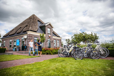 Personas paseando junto a bicicletas y una casa con techo de paja en Park Westerkogge, Holanda Septentrional.