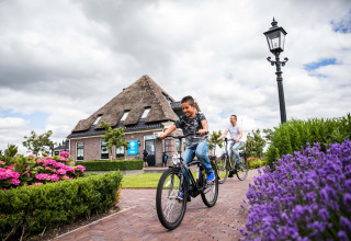 Deux personnes font du vélo sur une allée fleurie à Park Westerkogge, près d'une maison hollandaise traditionnelle.