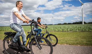 Dos personas montan en bicicleta por una carretera cerca de Berkhout, Países Bajos, con molinos de viento al fondo.