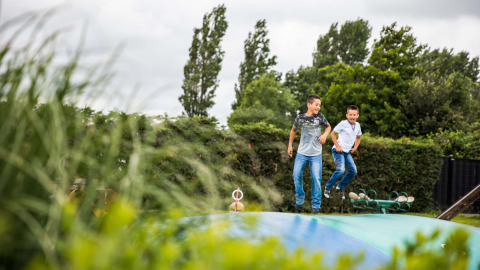 Zwei Jungen springen lachend auf einem großen Hüpfkissen im Park Westerkogge in Nordholland, Niederlande.