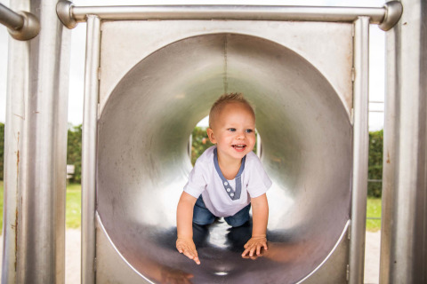Un jeune enfant souriant rampe dans un toboggan en métal à Park Westerkogge, un parc de vacances au Nord-Holland.