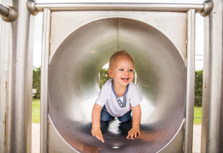 Un bambino felice gattona dentro uno scivolo di metallo nel parco giochi di Park Westerkogge, Olanda Settentrionale.