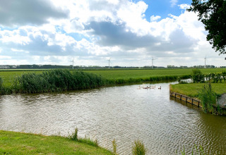 Landschap rond Berkhout, Noord-Holland met windmolens, rivier, zwanen en gedeeltelijk bewolkte lucht.