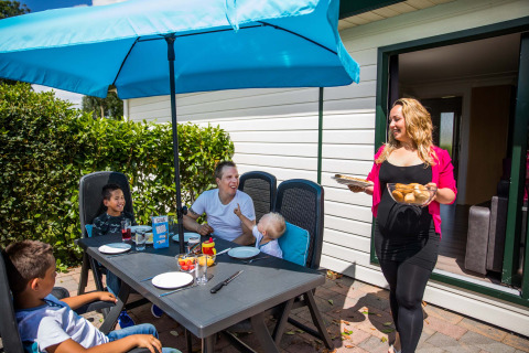 Familie nyder udendørs frokost under en blå parasol i Park Westerkogge, Nordholland, Holland.