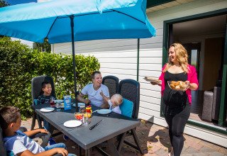Familie nyder udendørs frokost under en blå parasol i Park Westerkogge, Nordholland, Holland.