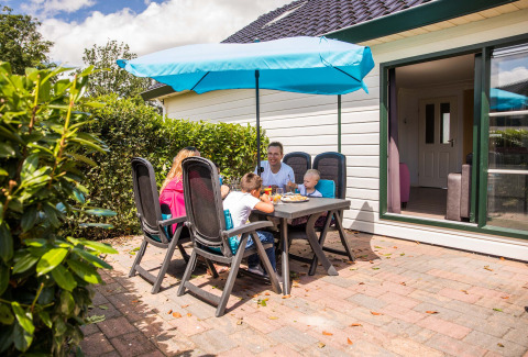 Familia desayuna al aire libre bajo sombrilla azul en Park Westerkogge, casa de vacaciones en Holanda Septentrional.