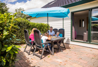 Familie nyder frokost på terrassen ved feriehus i Park Westerkogge, Nordholland, Nederlandene, solrig dag.