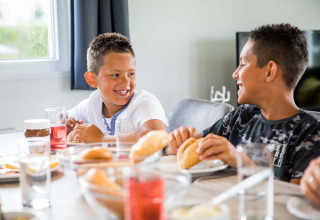 Twee jongens lachen en eten samen ontbijt aan tafel in Park Westerkogge, Noord-Holland, Nederland.