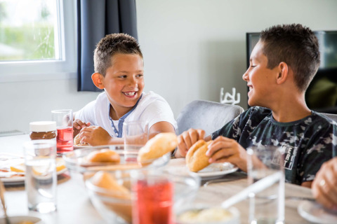 Twee jongens lachen en eten samen ontbijt aan tafel in Park Westerkogge, Noord-Holland, Nederland.
