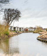 Billede af ferieboliger ved en kanal omgivet af græs og buske i Park Westerkogge, Nordholland, Holland.