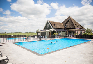 Buitenzwembad aan Park Westerkogge, vakantiedomein in Noord-Holland, Nederland, met rieten huis en weids uitzicht.