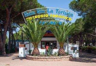 Entrance to Camping Village Baia Blu La Tortuga in Sardinia, Italy, surrounded by palm trees and forest.
